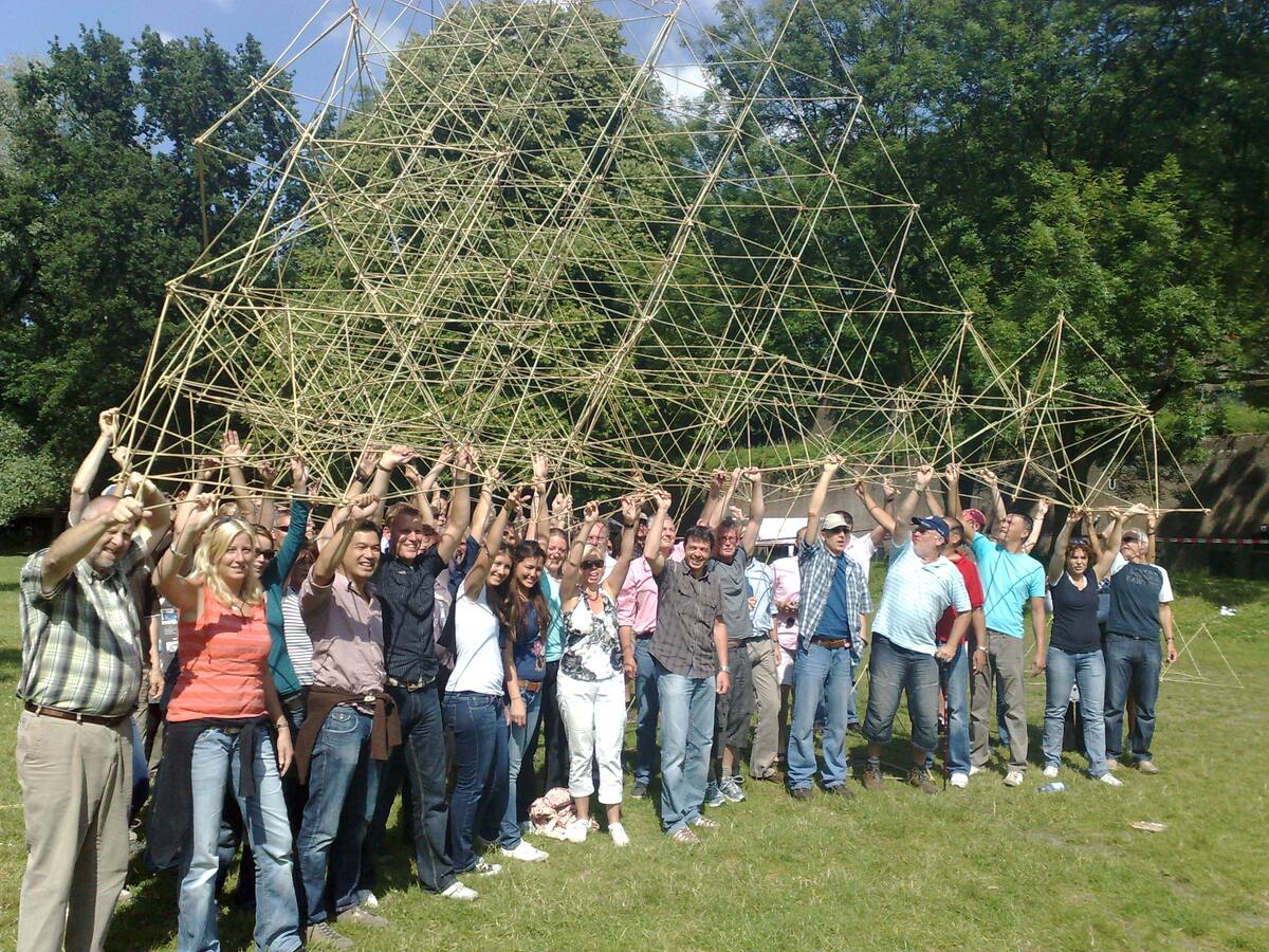 Team houdt samen een hoog bamboebouwwerk de lucht in tijdens de teambuildingactiviteit Bamboestieken