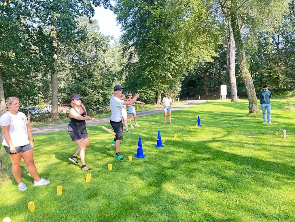 Groep kijkt toe terwijl een deelnemer vooraan de werpstok loslaat bij Kubb